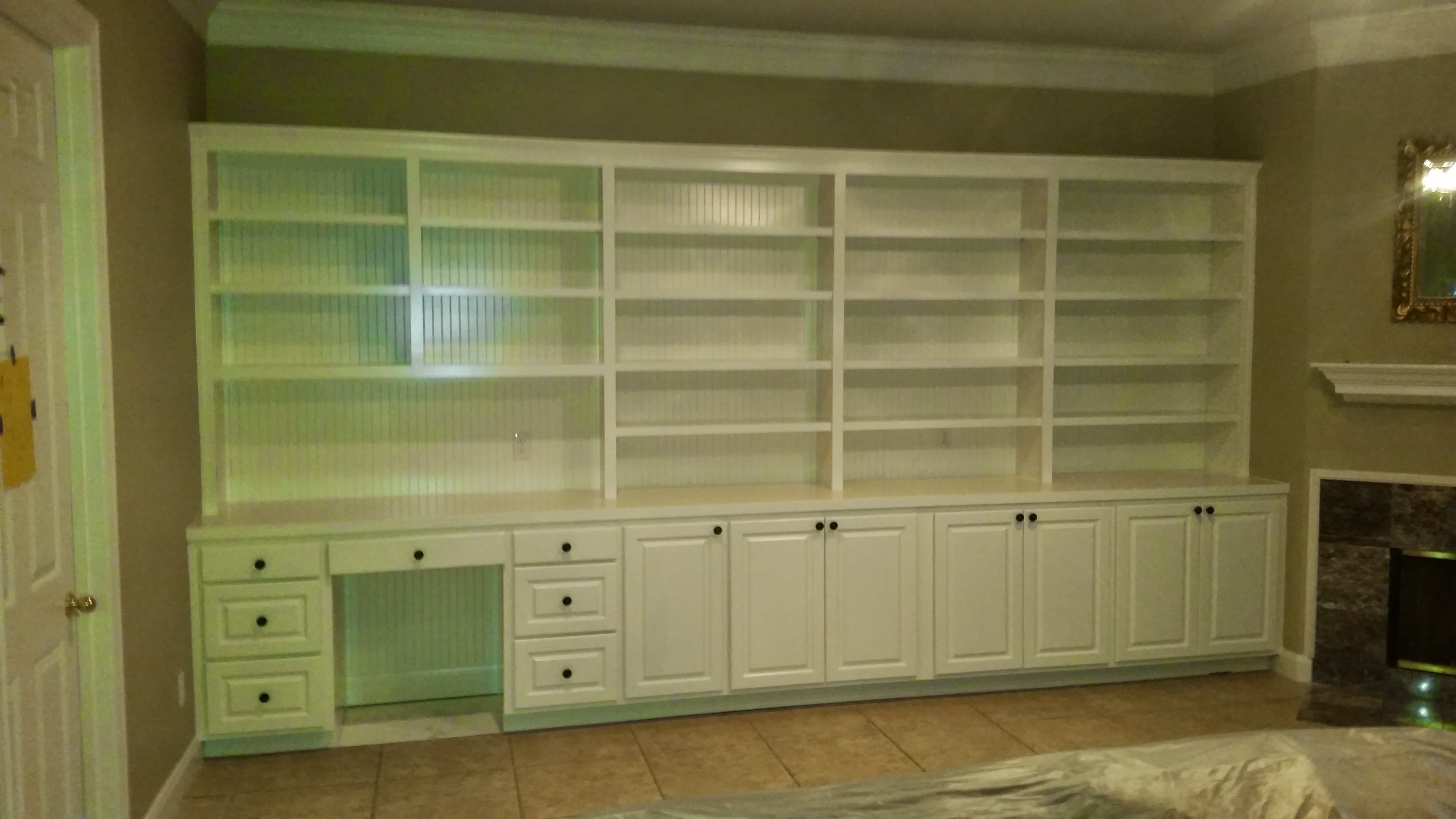 Finished floor-to-ceiling white built-in wall unit with shelving and lower cabinets