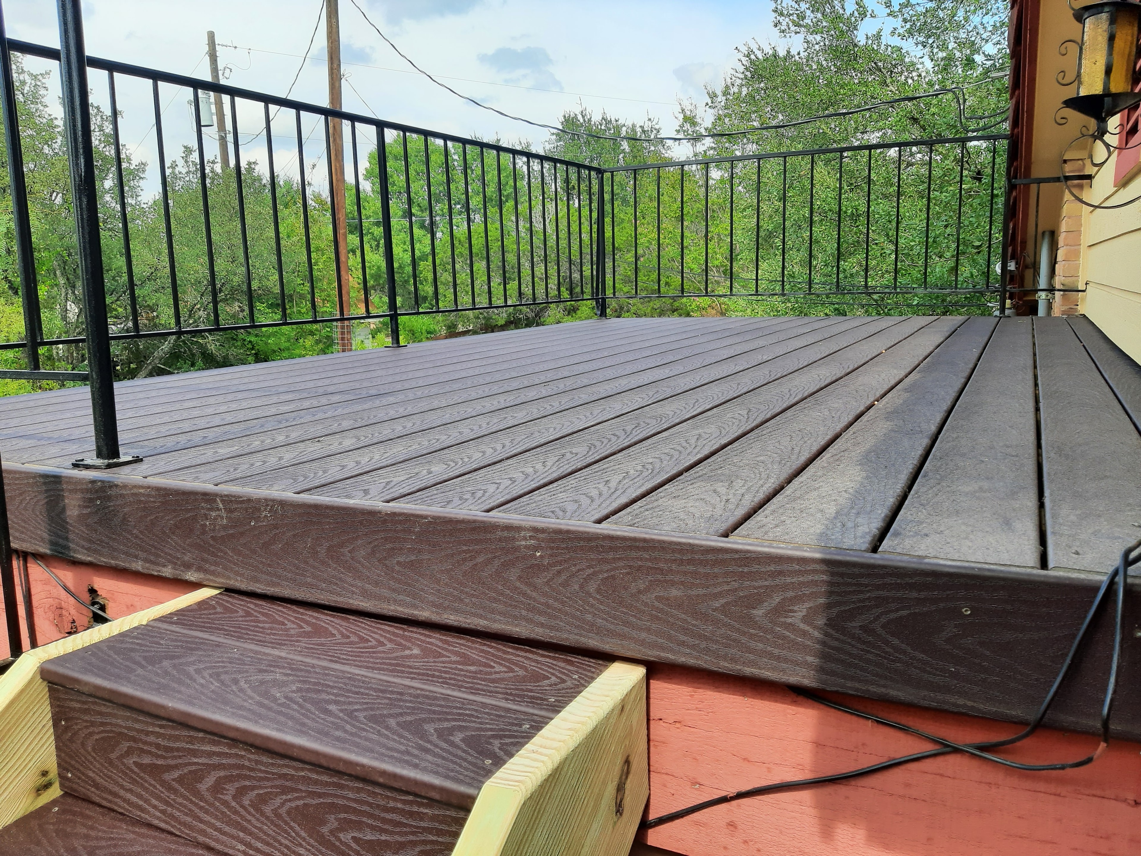 Finished composite deck with black metal railing and tree views