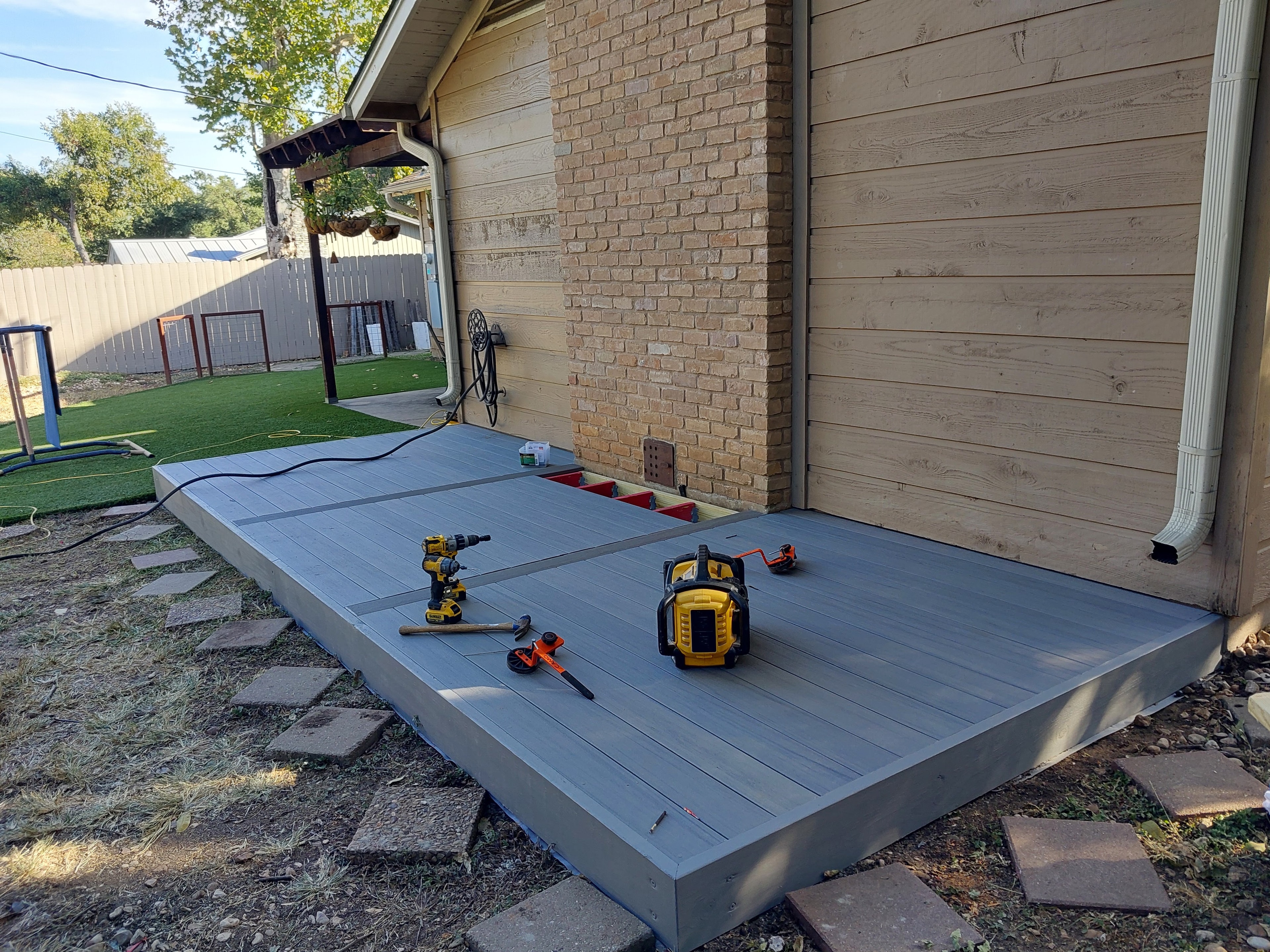Gray composite deck near completion beside brick home with artificial turf