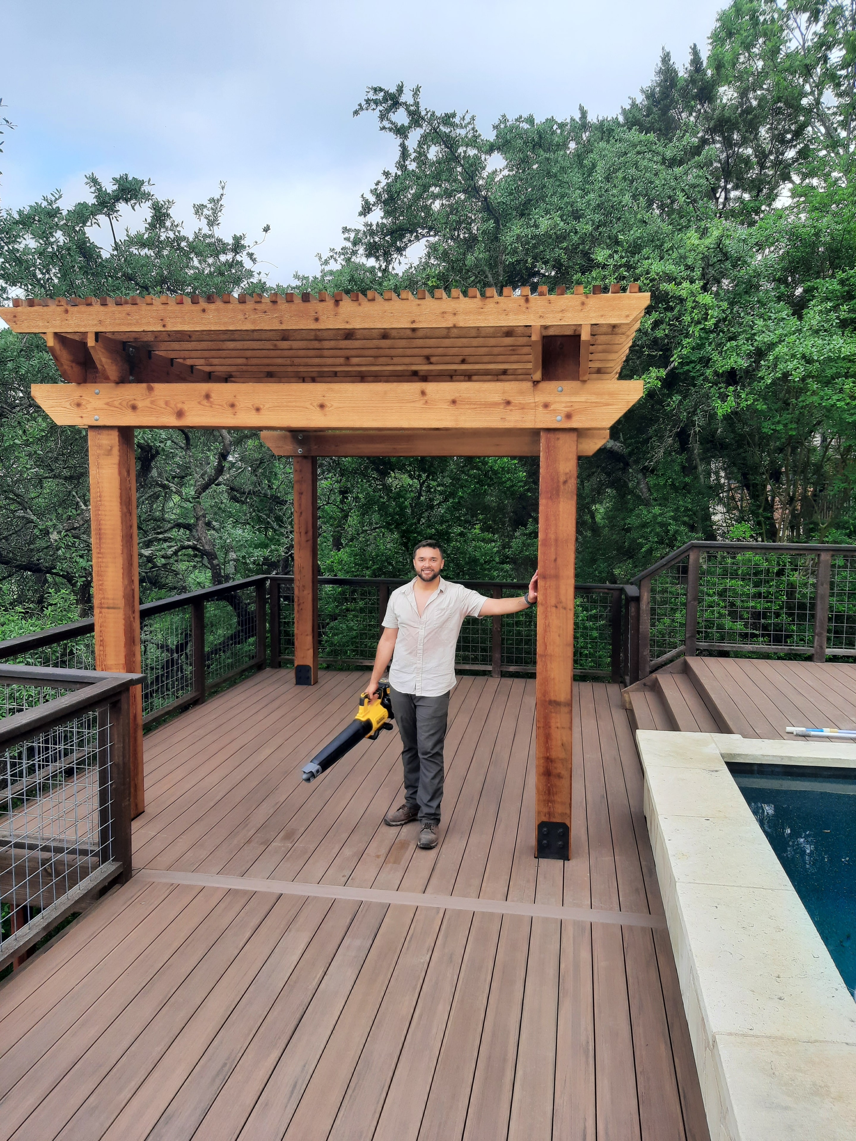 Yamil standing under cedar pergola on composite deck beside pool