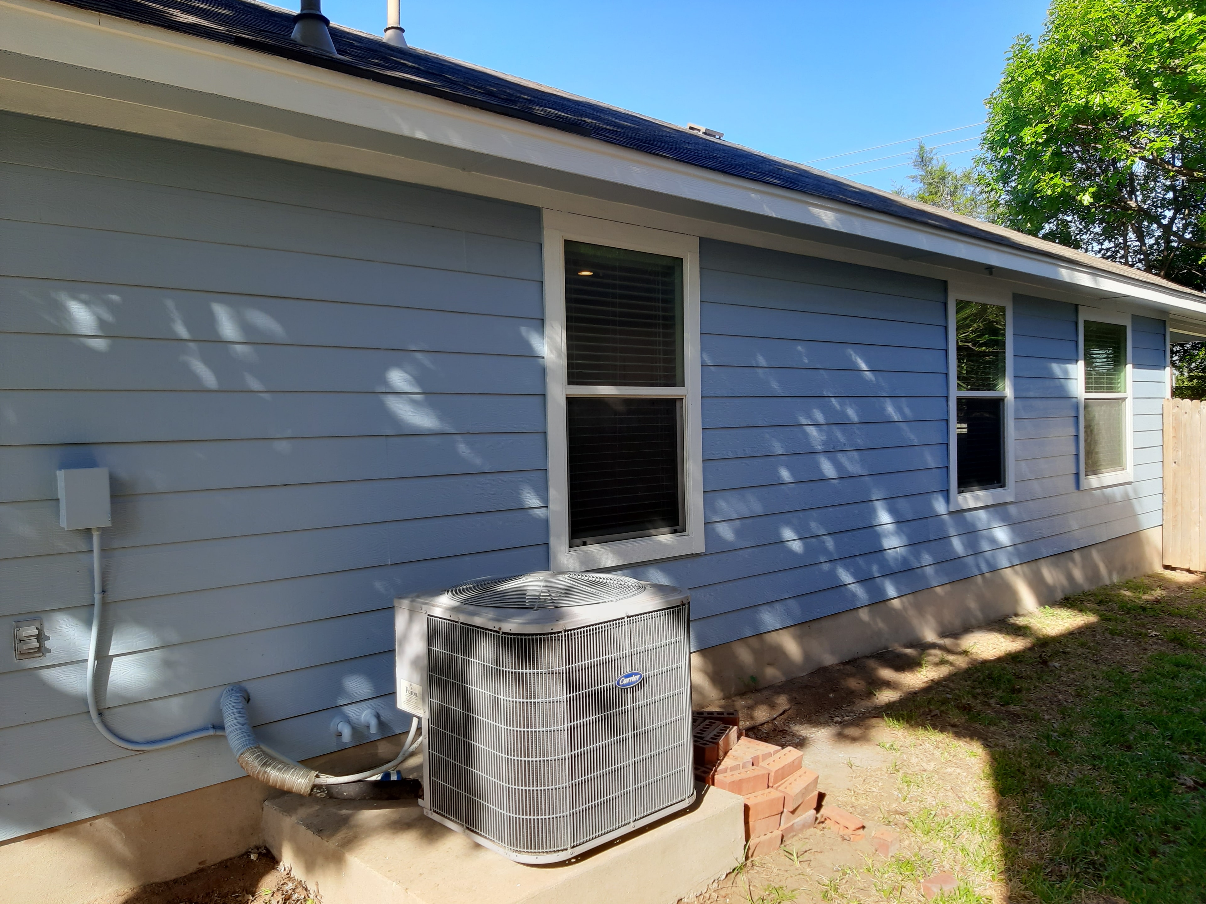 Freshly painted blue horizontal siding on home exterior with HVAC unit mounted on wall