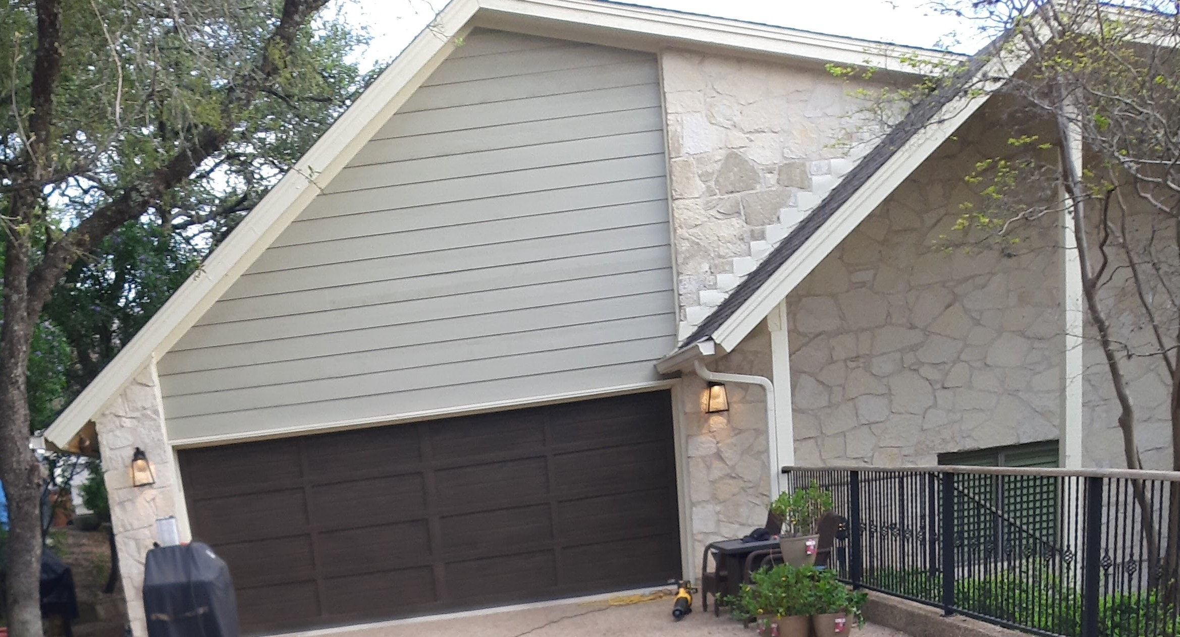 Painted gray horizontal siding on gable above garage with stone accent and dark garage door