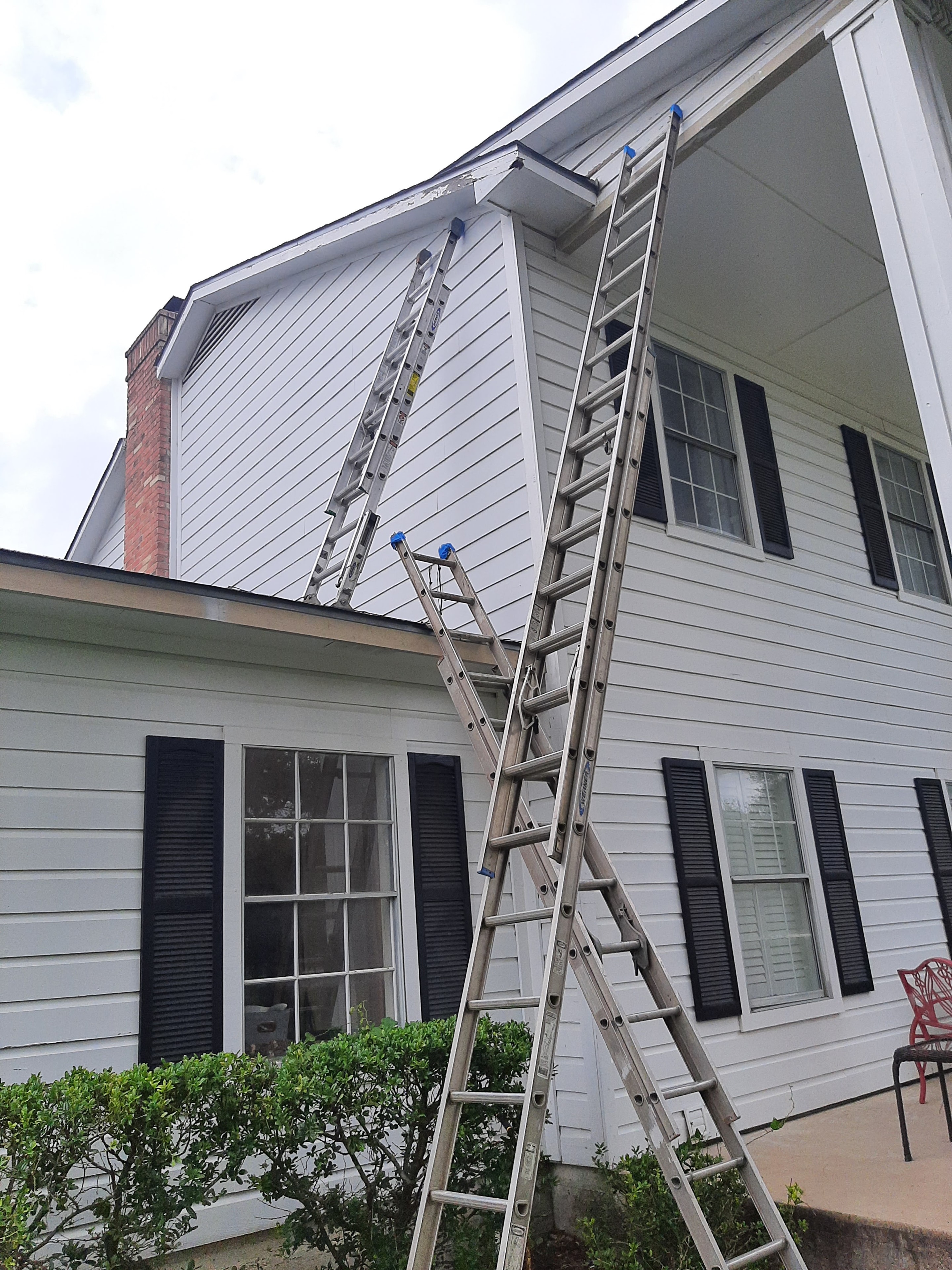 Two extension ladders set up against two-story white siding home with black shutters for exterior painting