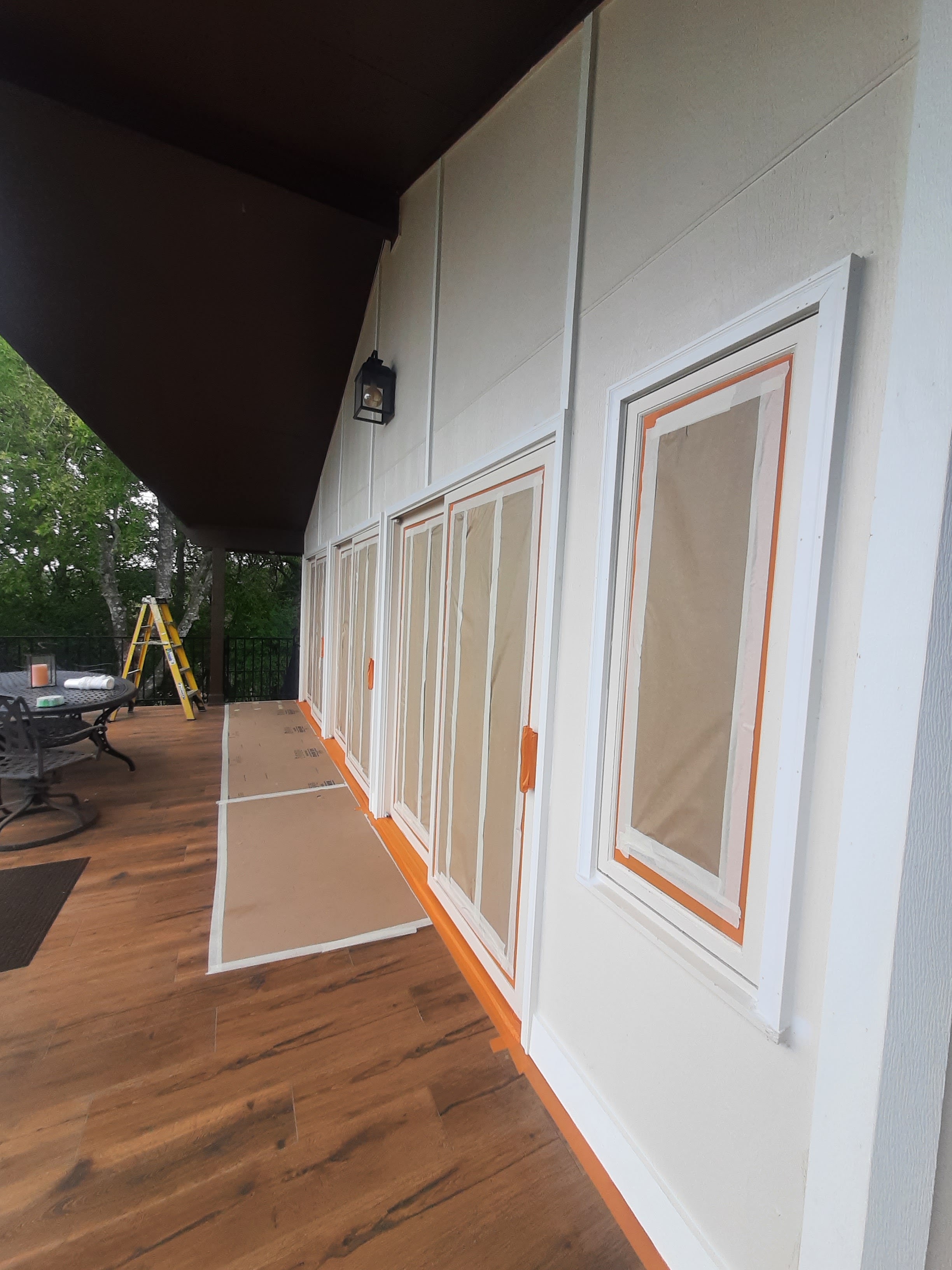 Exterior board-and-batten siding painted white with windows taped off for trim painting on covered deck