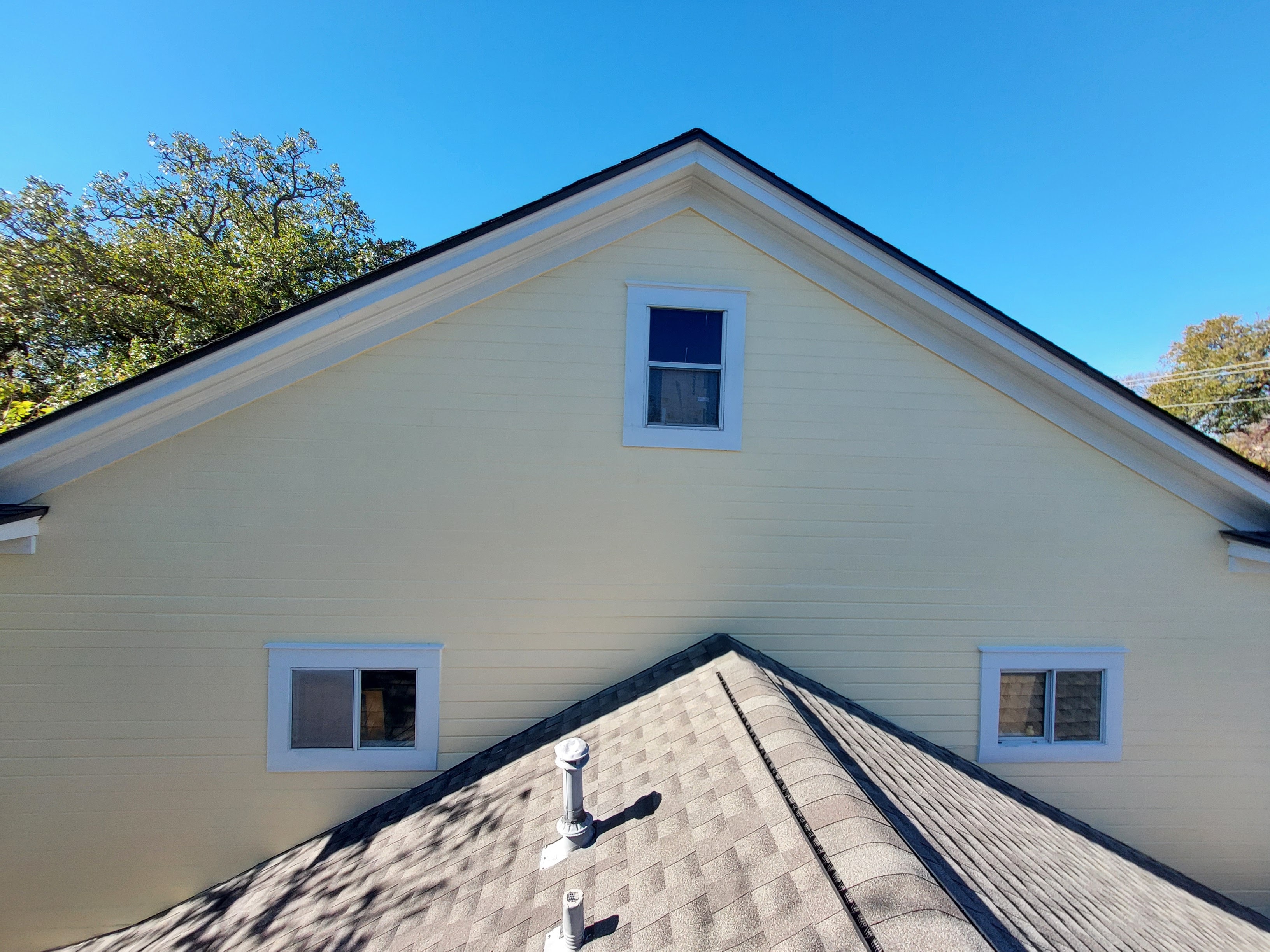 Freshly painted yellow gable and siding on home exterior viewed from roofline with white trim