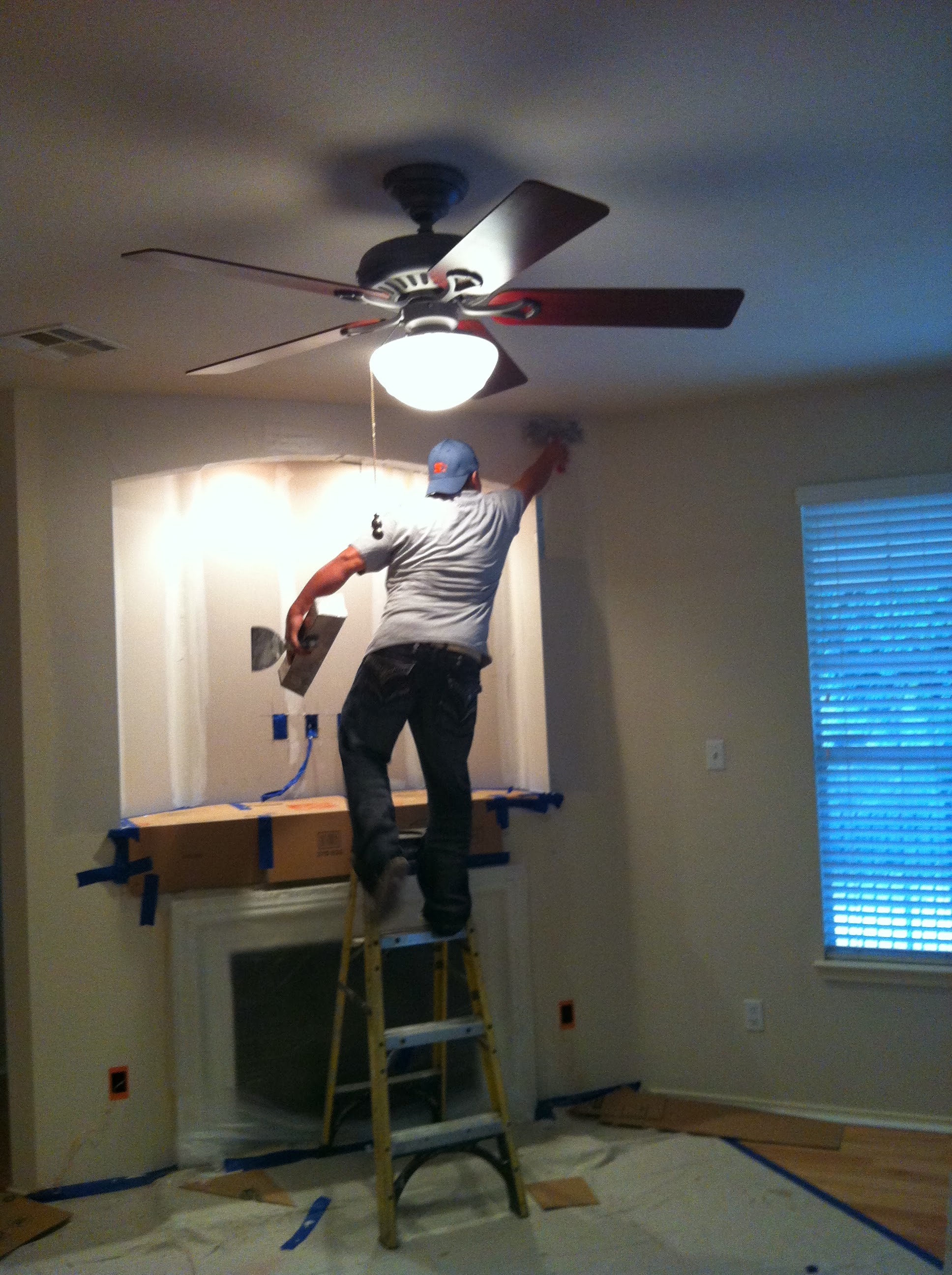 Painter on ladder cutting in around fireplace surround with ceiling fan above