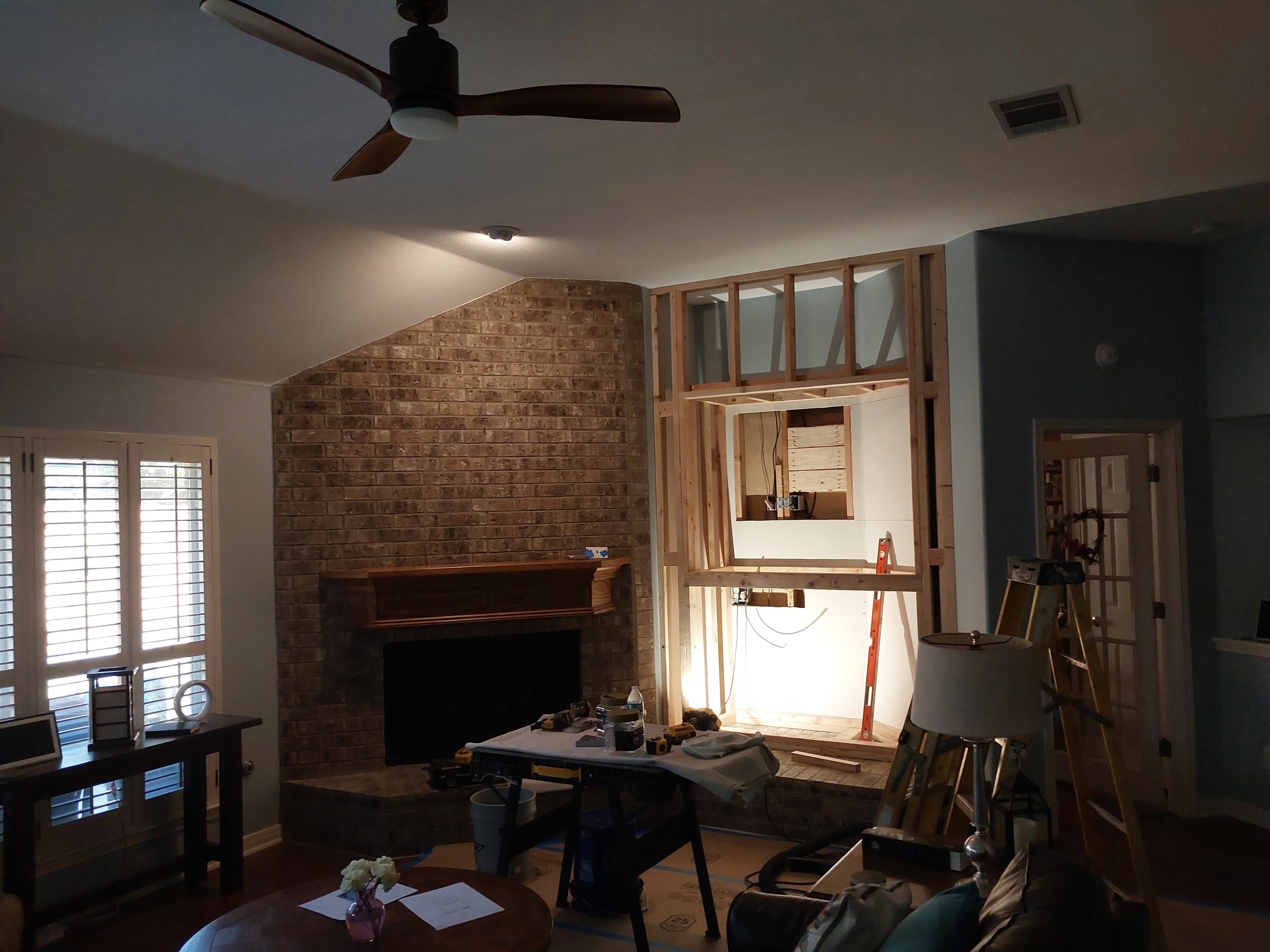 Living room remodel in progress with brick fireplace and new wall framing beside it