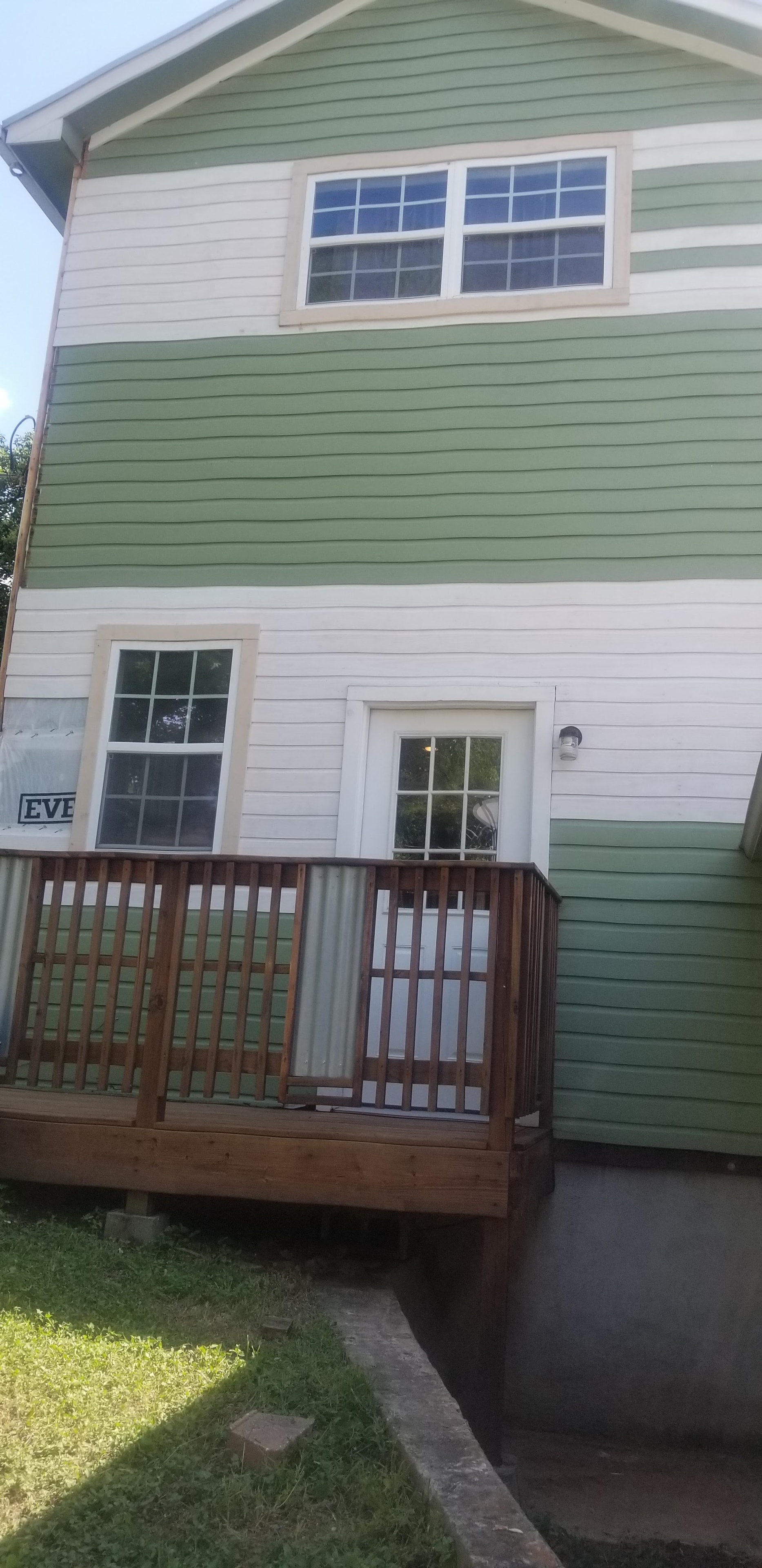 Two-story home with green and white horizontal siding and wood deck with railing