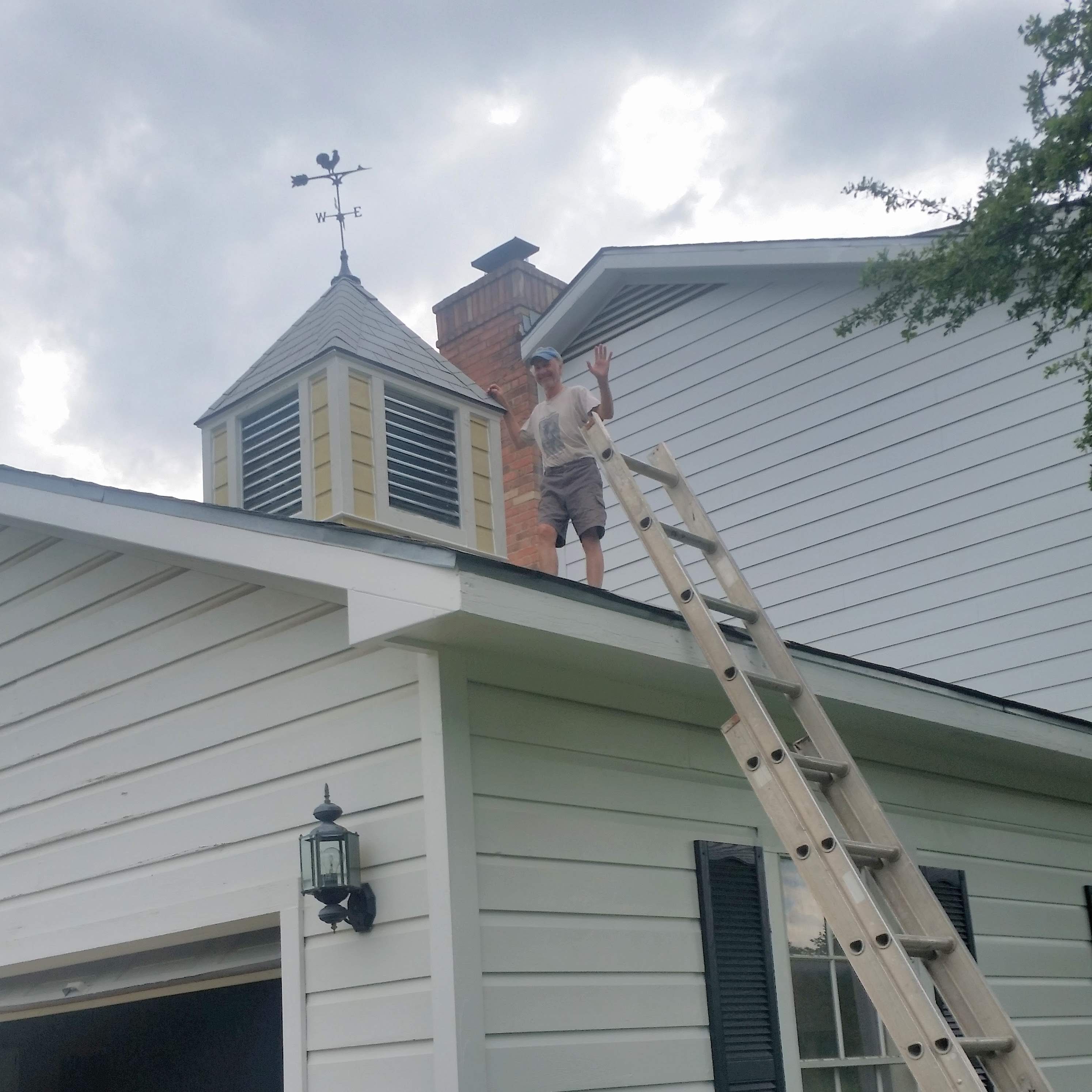 Yamil standing on rooftop beside cupola and chimney during siding repair on large two-story home