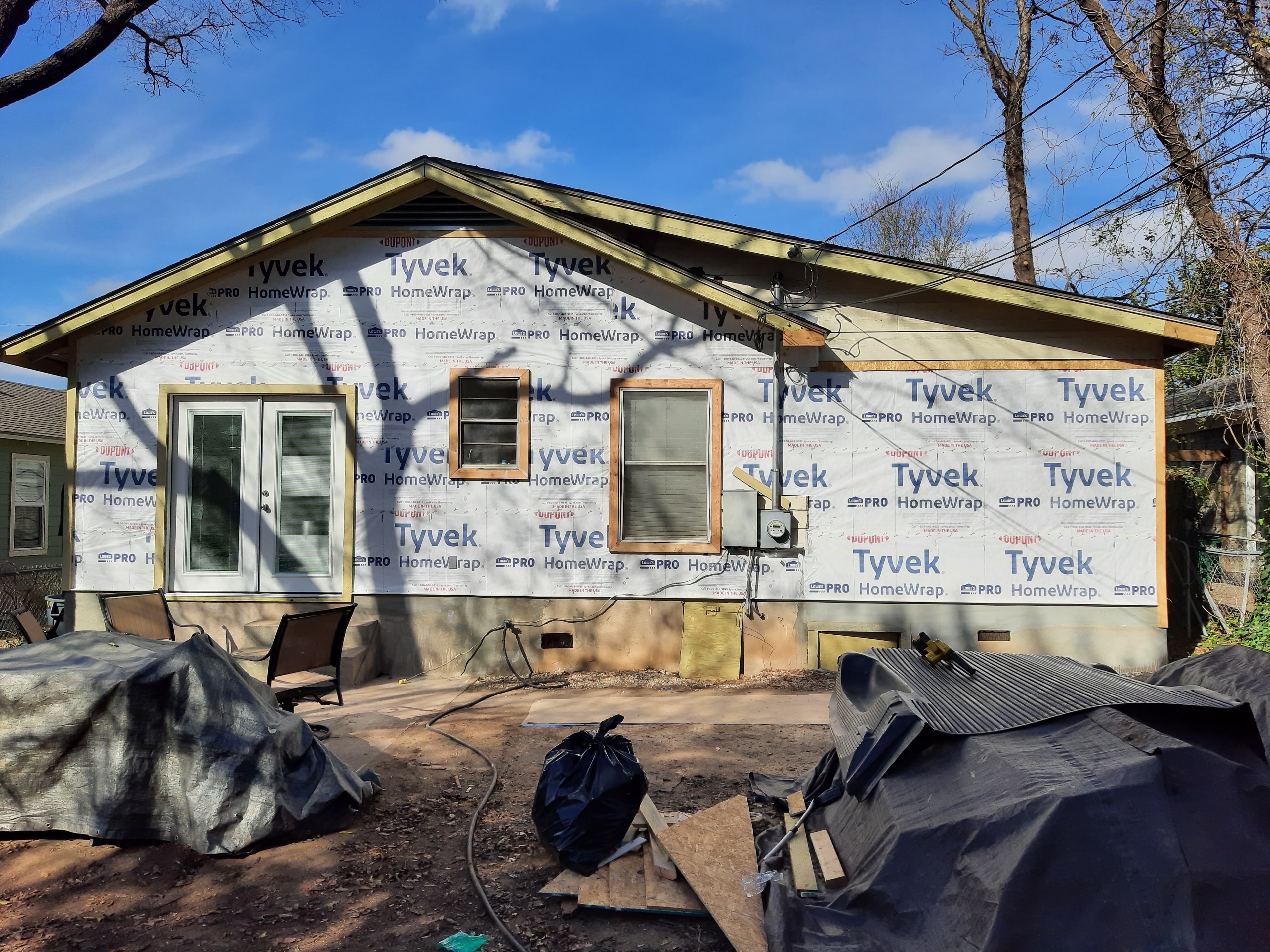 House exterior wrapped in Tyvek HomeWrap with windows framed out, siding removal in progress