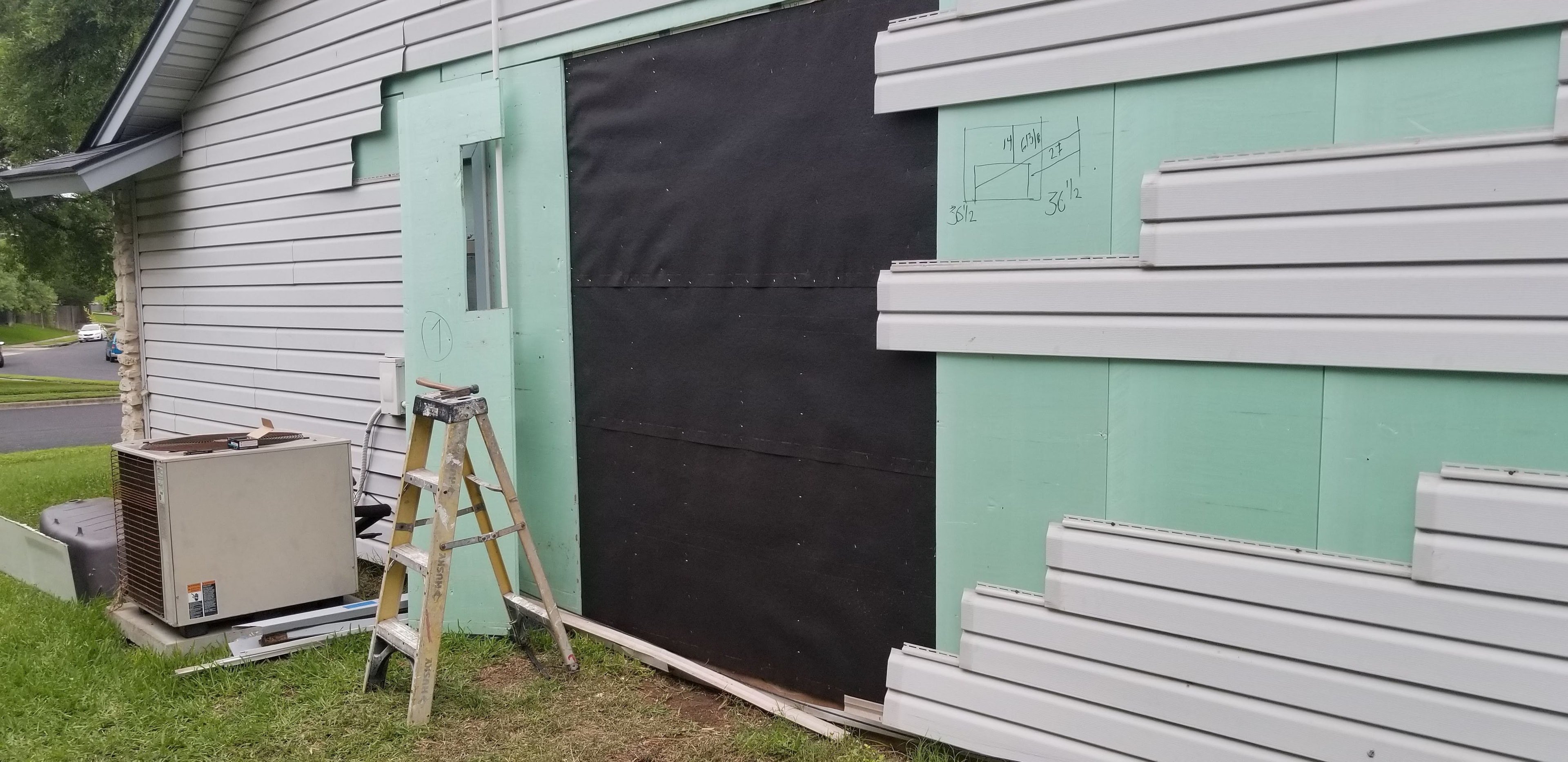 Vinyl siding installation in progress with green sheathing exposed and new panels staged beside HVAC unit