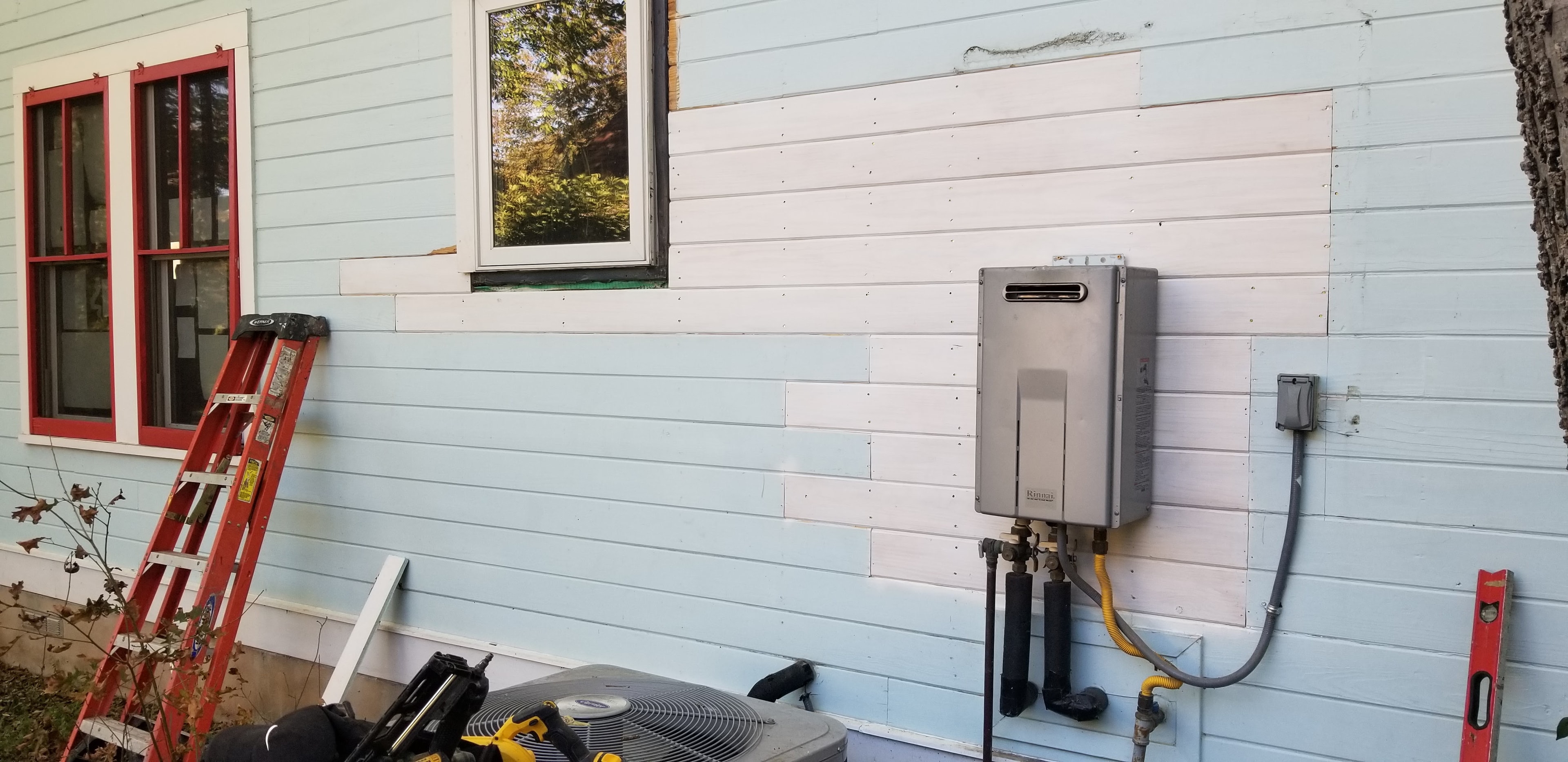 New white horizontal wood siding installed beside HVAC unit and tankless water heater with red-trimmed windows