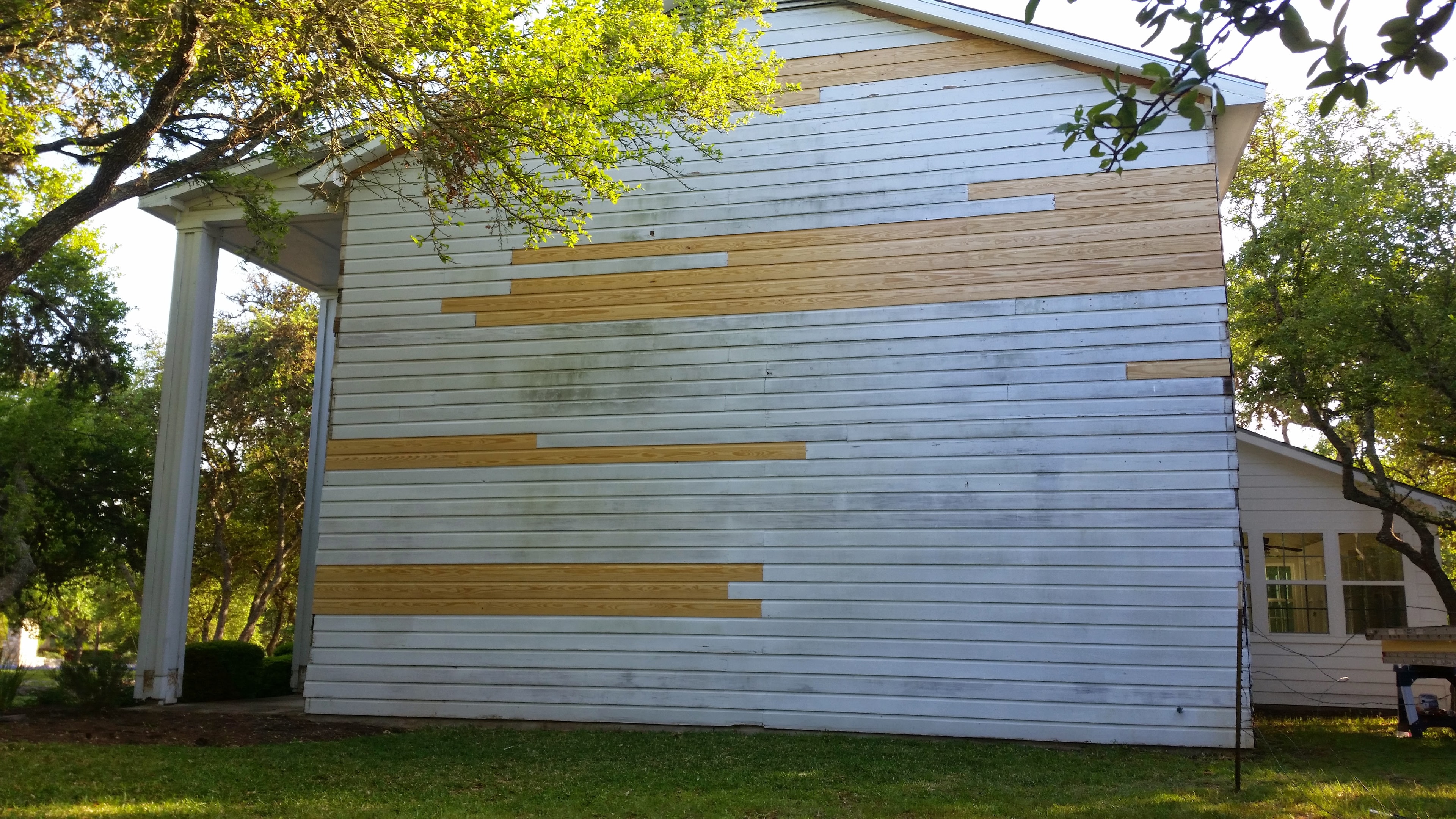 Wood siding board replacement in progress with new cedar boards patched into weathered white siding on two-story home