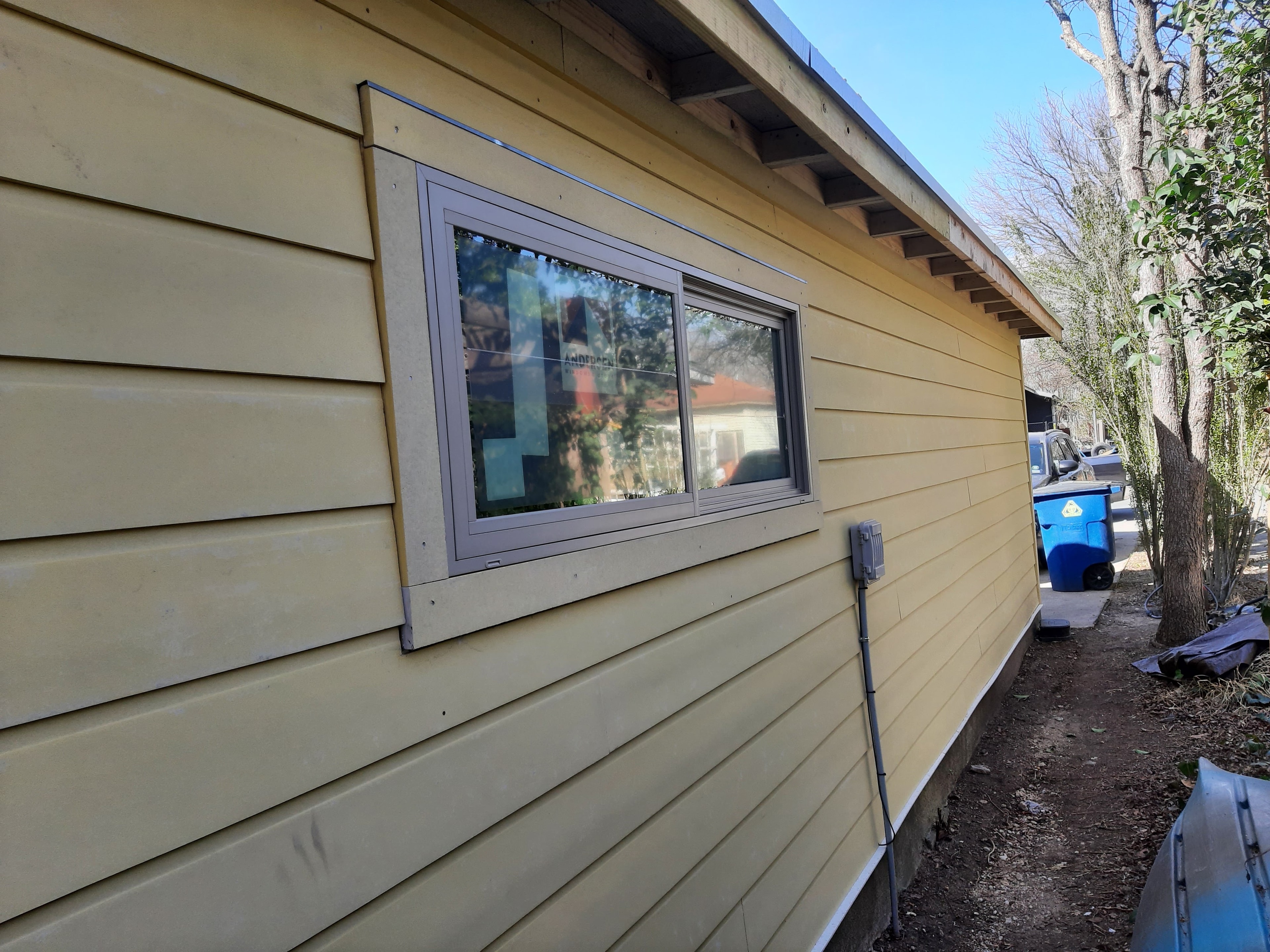 New yellow horizontal wood siding installed with Andersen window on home exterior