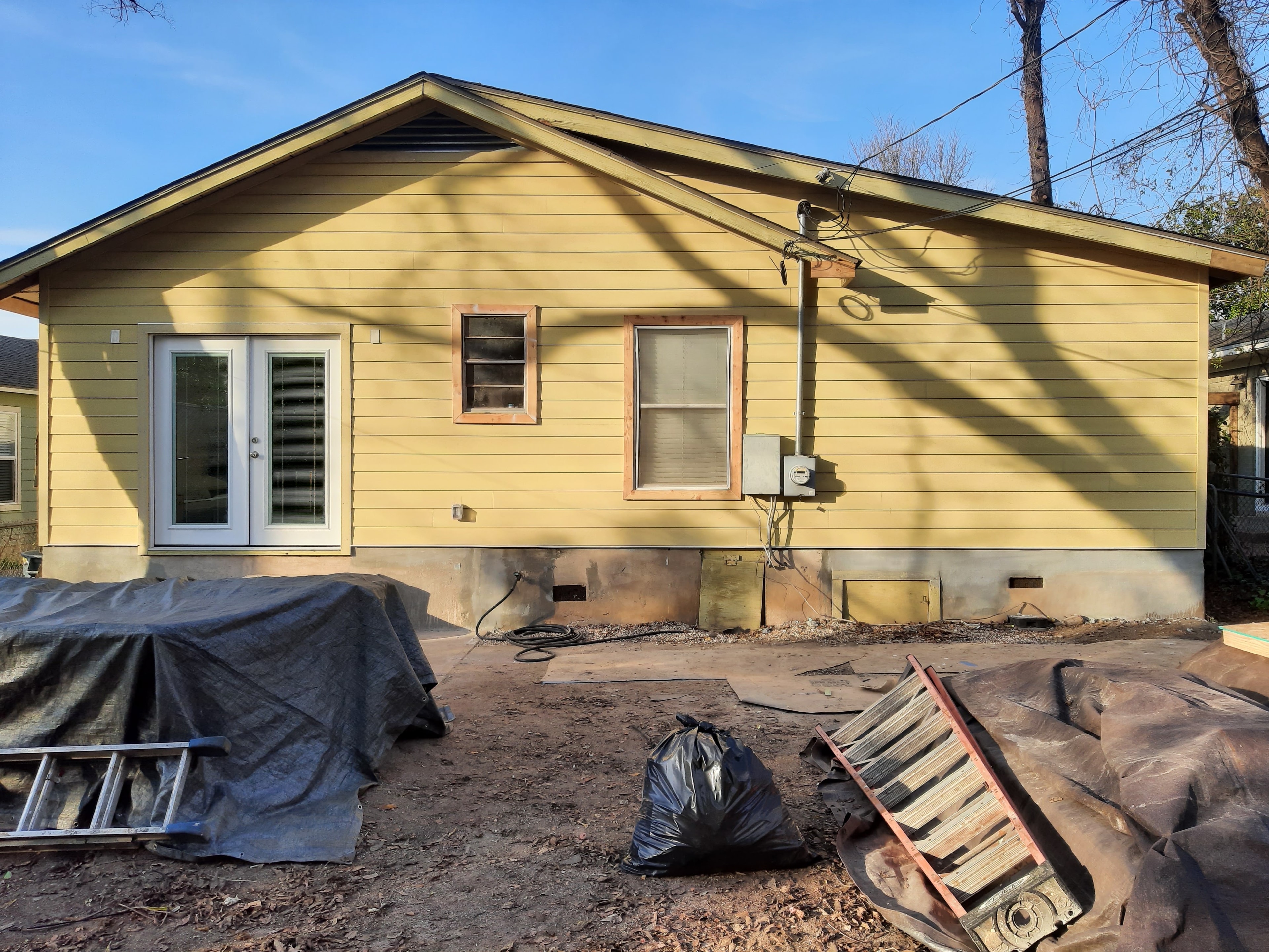 Rear of yellow house with new siding and windows complete, ladders and debris during cleanup