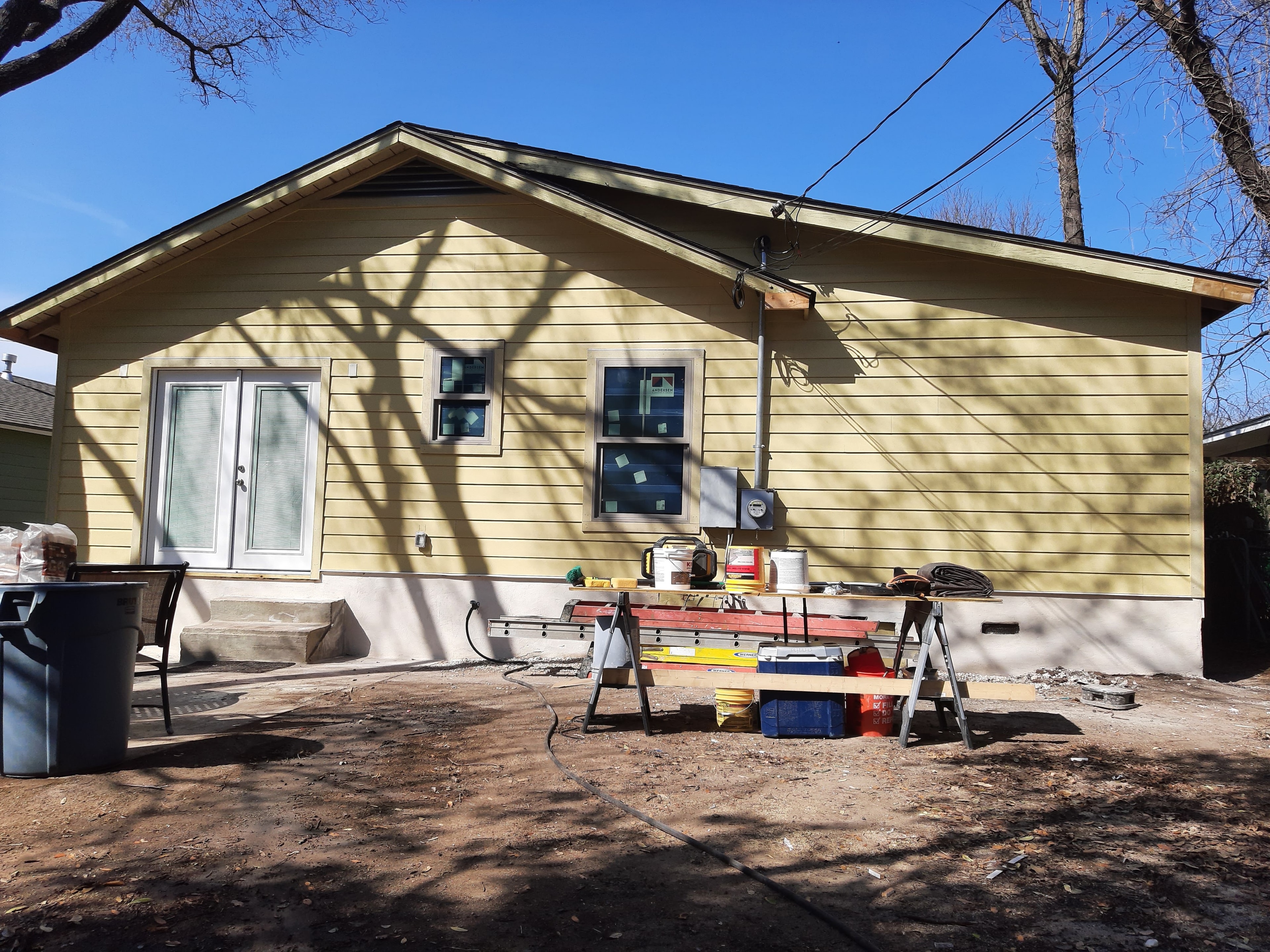 Rear of yellow house with new siding and windows installed, tools and sawhorses on job site