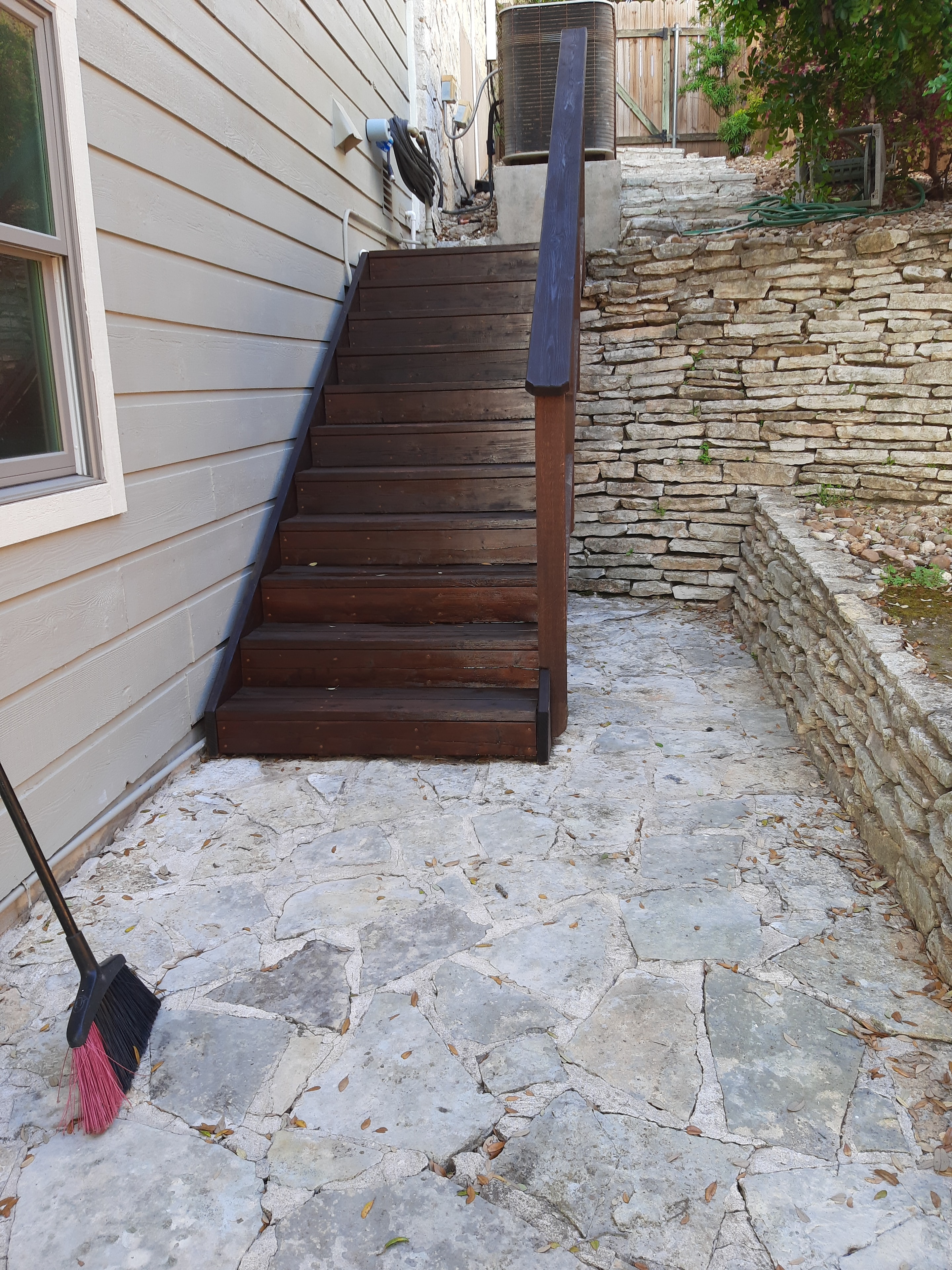 Stained wood railing panels against stone wall with composite deck and broom