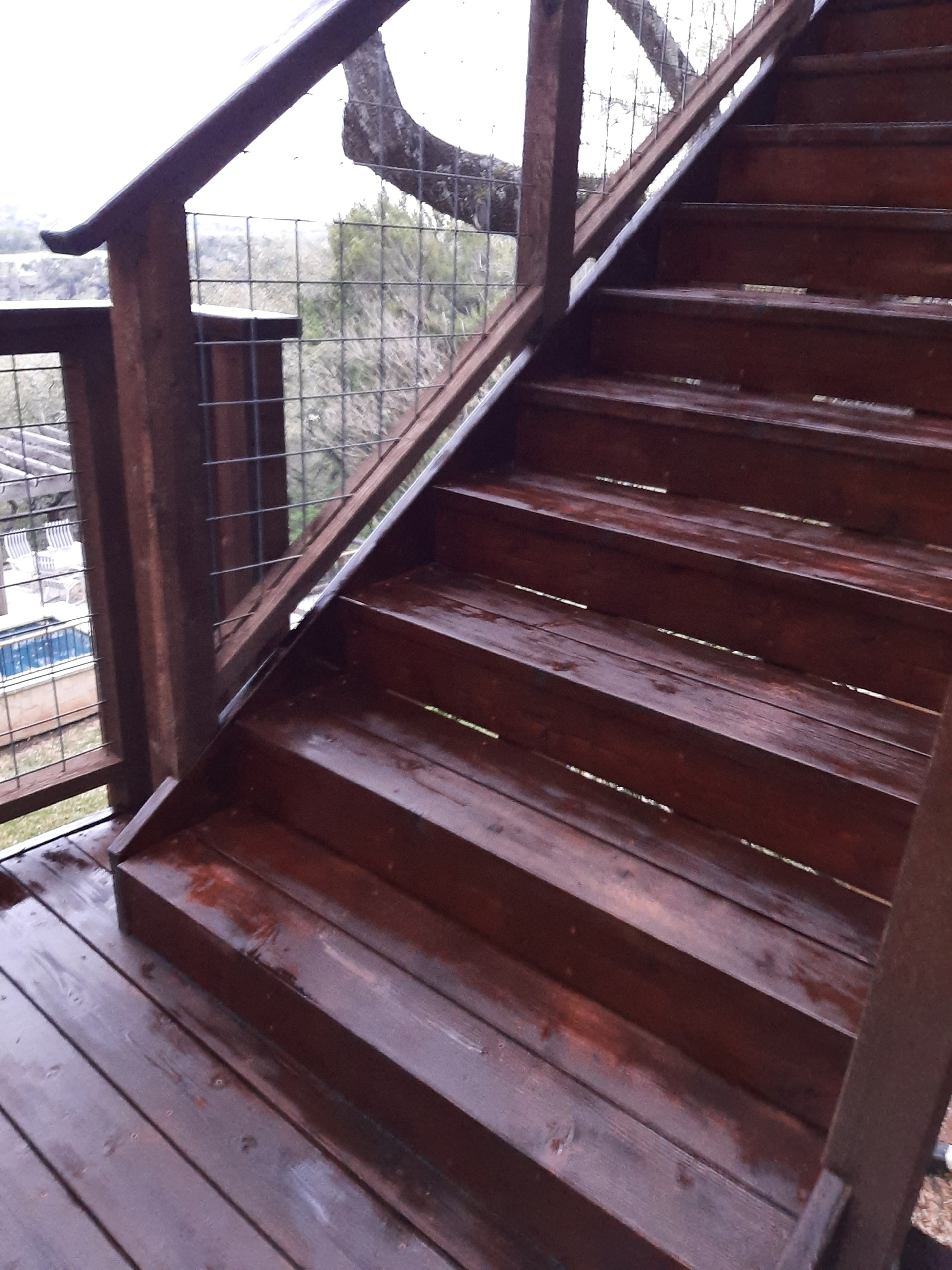 Stained wood deck beams and boards viewed from below with wire railing
