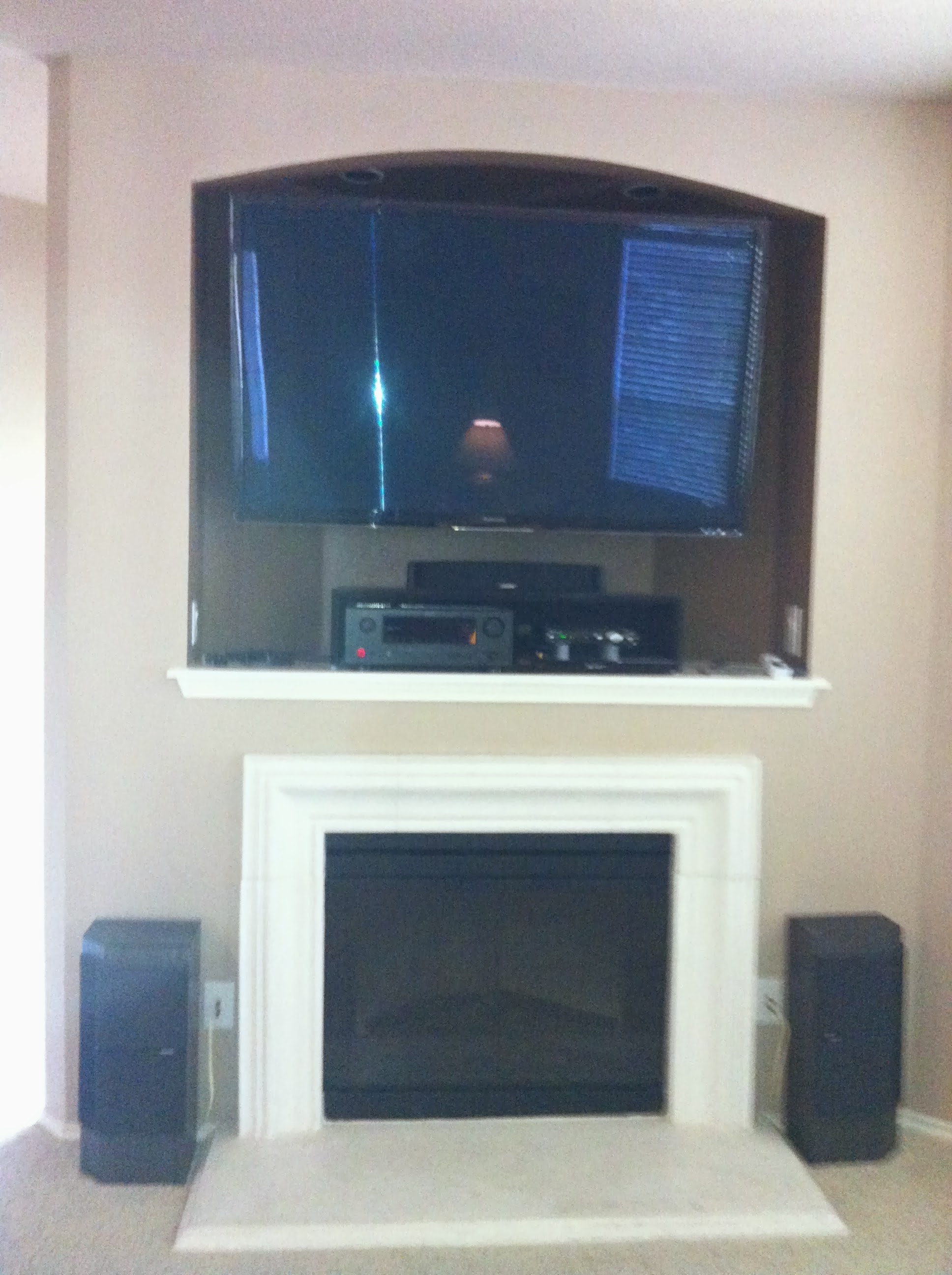 TV mounted in arched niche above fireplace with surround sound speakers and media equipment