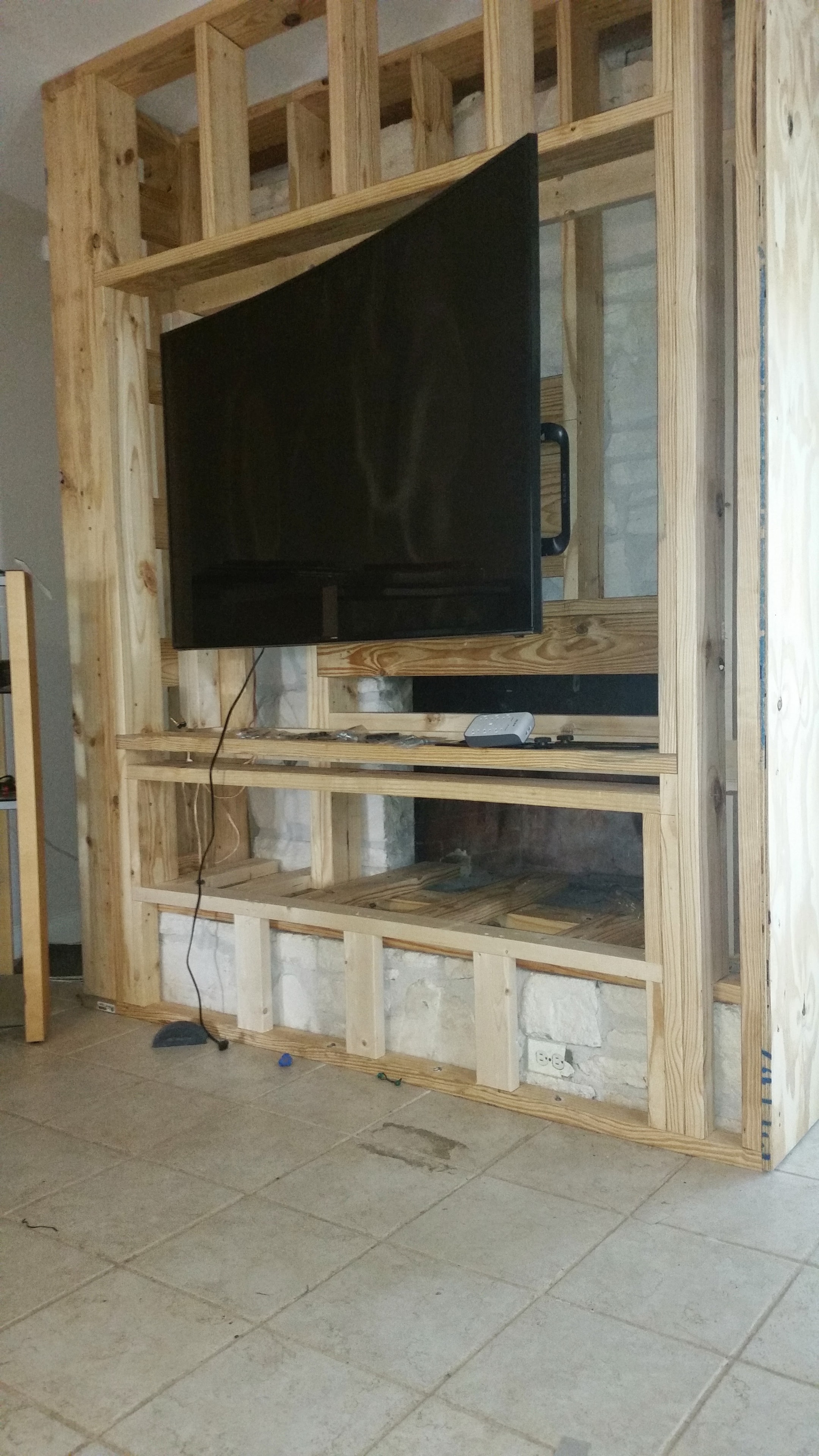 TV entertainment center built into old fireplace opening — wood framing in progress with flat-screen TV mounted