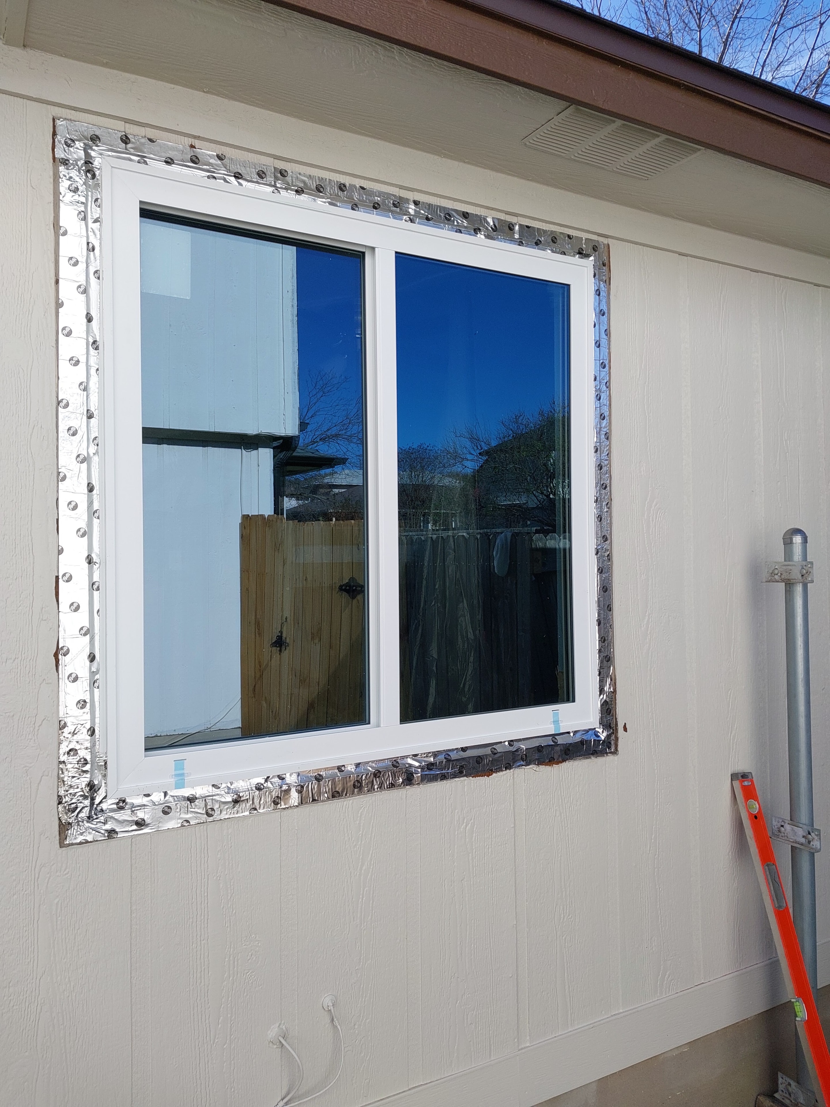 New white-frame window installed with metal flashing tape on house exterior
